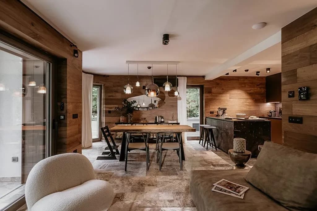 Modern living and dining area with wood paneling, stone floor, and contemporary lighting.