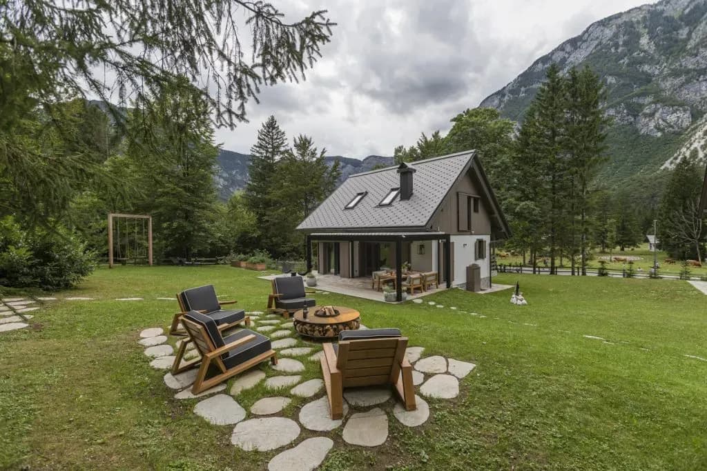 Modern cabin with outdoor seating area and fire pit, set against a backdrop of green mountains.