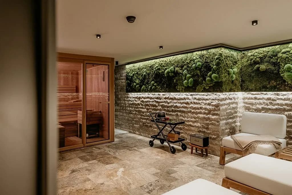 Sauna relaxation area with stone wall, preserved moss feature, and white lounge chairs