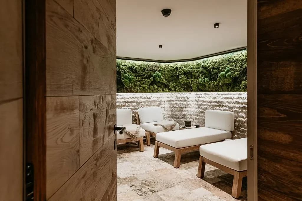 Relaxation room with white loungers, stone wall, and illuminated vertical moss garden view through doorway.