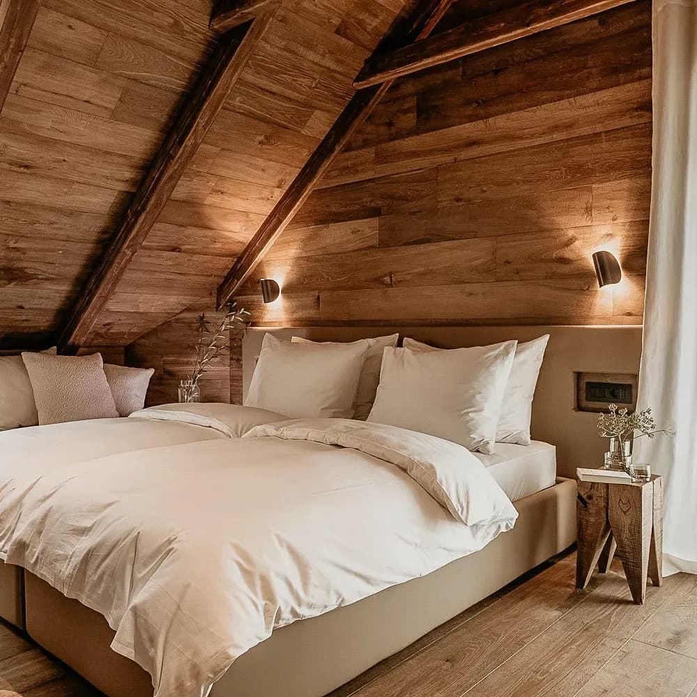 Cozy attic bedroom with wood paneling, white bedding, and rustic side table lighting