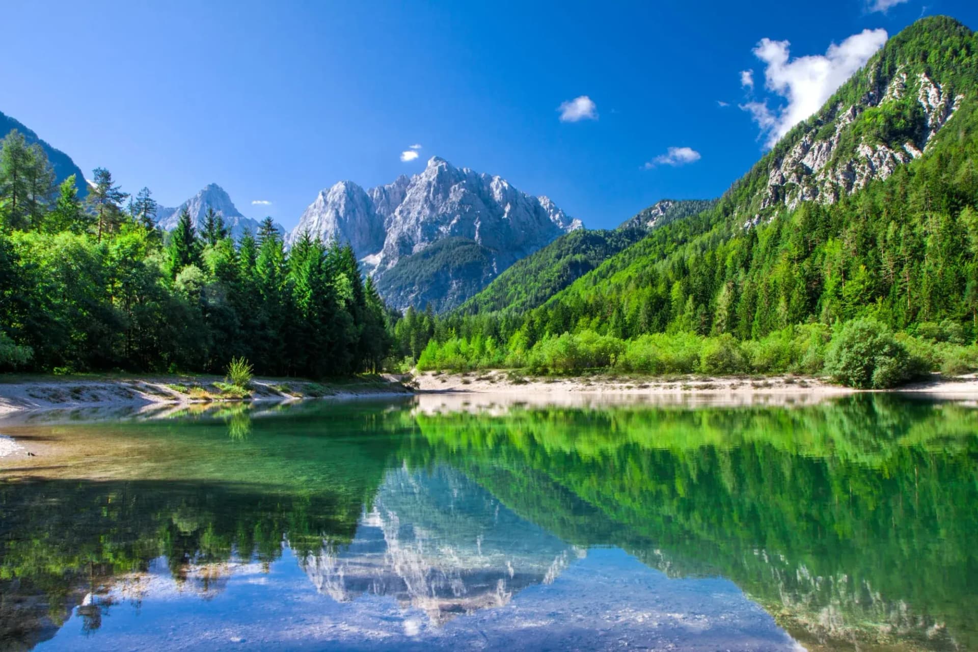Mountain reflection in clear green lake surrounded by dense green forest under blue sky
