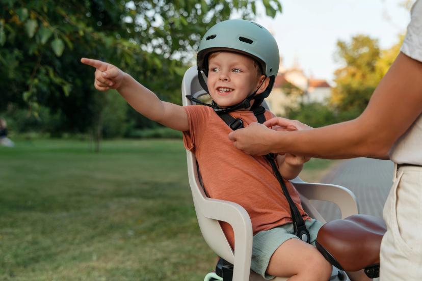 A smiling child being secured in a bicycle seat by a parent, ready for a safe outdoor ride and adventures.