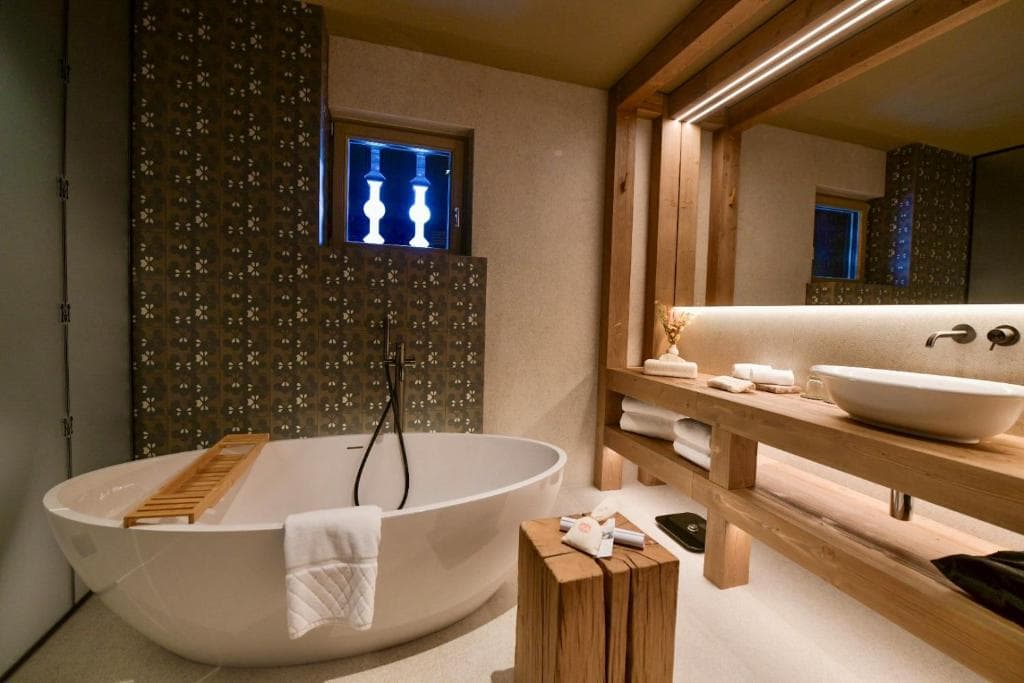 Modern bathroom with a freestanding white bathtub, wooden vanity, and patterned tile wall.
