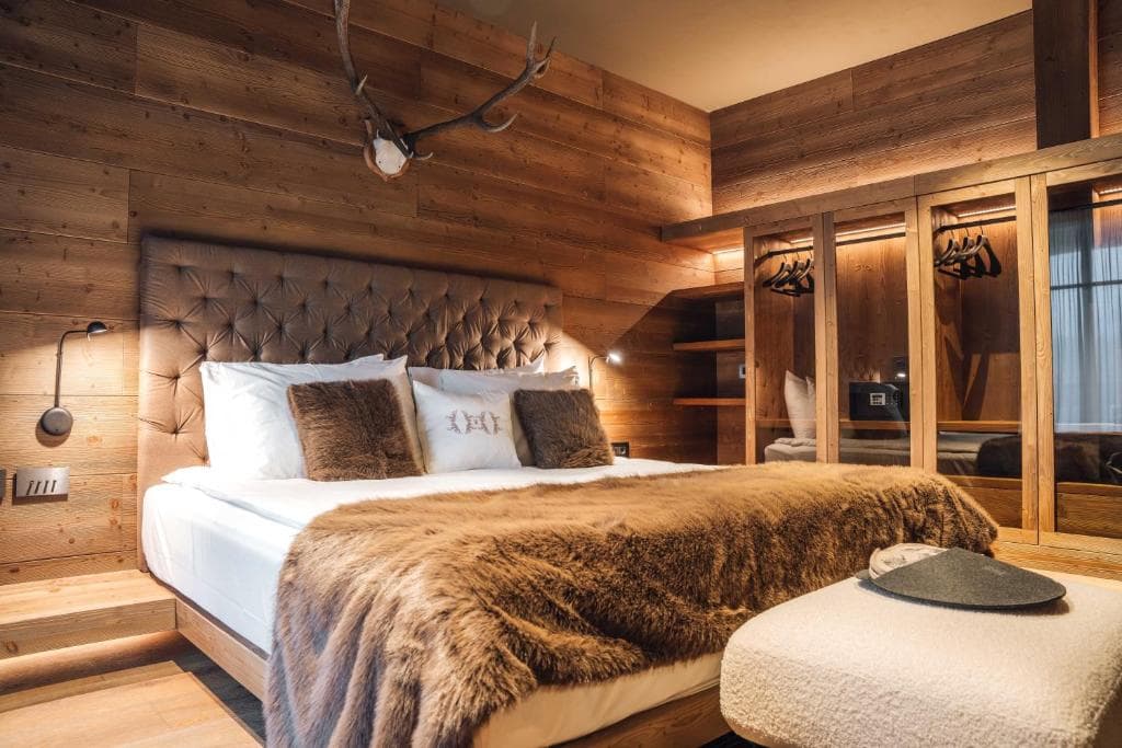 Bedroom with wooden walls, tufted headboard, and faux fur throw in an alpine-style room.