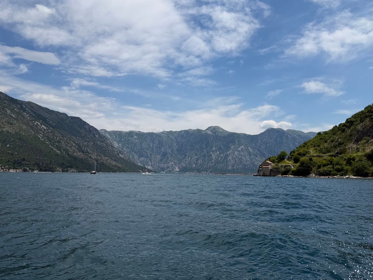 Boats on coastal waters surrounded by steep mountains under a cloudy sky